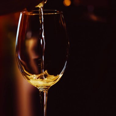 Işıklı şarap bardağı masanın üzerinde duruyor ve içine pembe şampanya damlatı. Metin için yer. Düşük anahtar