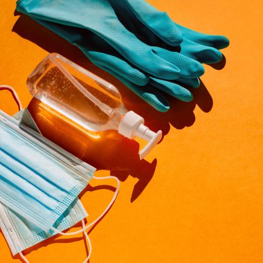 Personal protection kit when leaving the house during a coronavirus pandemic: individual face masks, gel sanitizer and hand gloves. Orange background, trend light, contrasting shadows. Top view. clipart