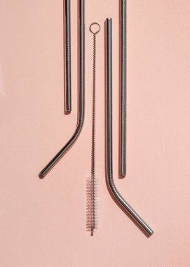 Pembe arka planda yeniden kullanılabilir kokteyl tüpleri ve temizlik fırçaları. Sıfır israf kavramı. Yukarıdan manzara. Dikey biçim.