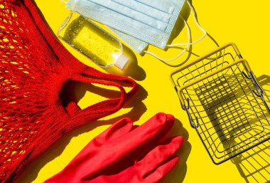  Yeniden kullanılabilir kırmızı alışveriş torbası, tek kullanımlık eldiven, dezenfektan ve metal alışveriş sepeti. Koronavirüs salgını sırasında dükkânı ziyaret etmek için gerekli malzeme. Plastiğe karşı sıfır atık. Üst görünüm.