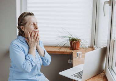 Evde online dersler var. Yaşlı beyaz bir kadın dizüstü bilgisayarın önünde yüz bakımı yapıyor. Bir salgın sırasında sağlığınıza dikkat etmek.