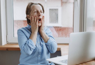 Evde online dersler var. Yaşlı beyaz bir kadın dizüstü bilgisayarın önünde yüz bakımı yapıyor. Bir salgın sırasında sağlığınıza dikkat etmek.