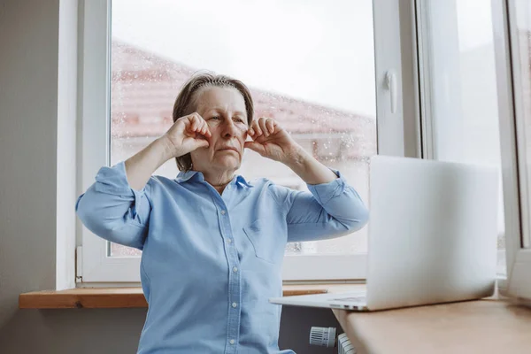 Anti-aging and facial wrinkles. An older woman looks at a guide to anti-aging face lifting with exercises and repeats them in front of the computer.