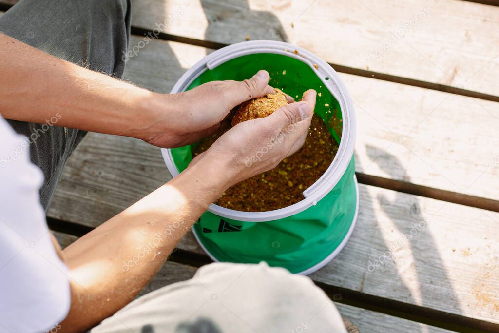 The fisherman picks up the bait for the fish from the bag. Hands close up