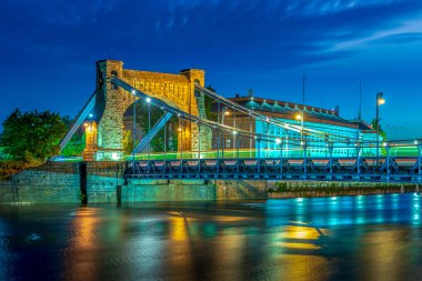 Grunwald Köprüsü. Wroclaw, Polonya 'da Grunwaldzki asma köprüsü. Hızlı hareket eden arabalarla alacakaranlıkta, tramvaylar trafik ışığı yolları oluşturuyor. Şehrin en bilinen simgesi banka tarafından görüldü.