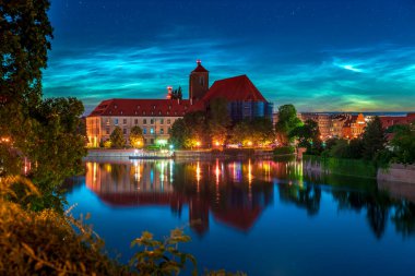 Dünya 'nın üst atmosferinde Wroclaw üzerinde gece manzarası gece manzarası gece bulutları (NLC). Güzel gece parlayan bulutlar ve yıldızlar şehrin tarihi simgelerinin üzerinde ve gün batımında nehirde yansıyor.