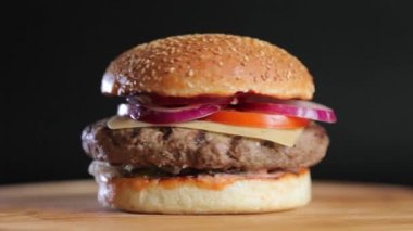 Bir büyük pirzola, peyniri, salatalık, domates, soğan, lahana, sos ve susam tohumu siyah bir arka plan ile topuz ile sulu hamburger