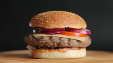 Bir büyük pirzola, peyniri, salatalık, domates, soğan, lahana, sos ve susam tohumu siyah bir arka plan ile topuz ile sulu hamburger