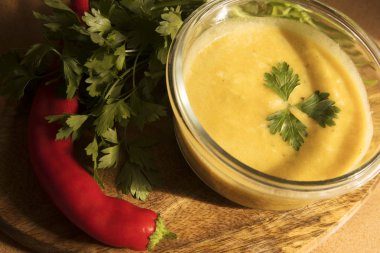 Mercimek krem çorba sarı renkli yeşillik ve sıcak biber bir ahşap tahta üzerinde yanındaki şeffaf tabak