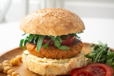 Ev yapımı mayalı çörek, domates, salatalık turşusu ve ahşap bir tabakta roka ile vejetaryen falafel humus burger.