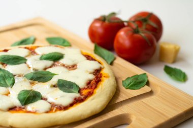 Domates soslu ev yapımı İtalyan Napoli pizzası mozzarella peyniri ve fesleğen yaprakları: pizza Napoletana. Domates, peynir ve fesleğen yapraklarıyla çevrili ahşap bir kesim tahtasının üzerinde.