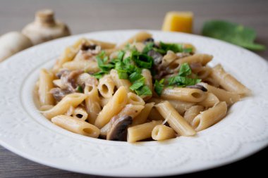 Kırmızı soğanlı vejetaryen kremalı sarımsaklı makarna. Beyaz bir tabakta fesleğenle süslenmiş. Malzemeleri arka planda, gri ahşap yüzeydeki her şey.
