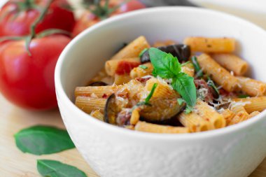 Geleneksel İtalyan yemeği: domatesli makarna, patlıcan, sarımsak, fesleğen ve ricotta peyniri ahşap kesim tahtasının üzerinde.