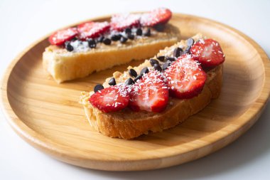 Fıstık ezmeli tost, çikolata parçacıkları, çilek, hindistan cevizi gevreği ve ahşap tabakta ev yapımı ekmek.