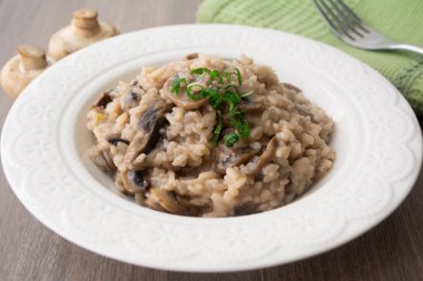 Klasik İtalyan vejetaryen mantarlı risotto arborio pilavı, mantar, soğan ve sarımsaklı fesleğen kurdeleli yeşil peçeteli ve çatallı.