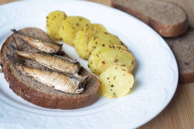 Çavdar ekmeğine konserve sprat konservesi ve fırında patates.