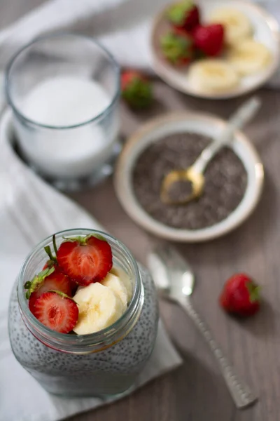 Healthy vegan chia seed pudding in a mason jar topped with strawberry and banana. Rustic and dark concept