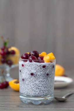 Taze kayısı ve vişneli chia tohumu pudinginin sağlıklı vejetaryen kahvaltısı. Ahşap arka planda daha fazla meyve ve kaliteli gümüş kaşık. Kırsal ve koyu estetik