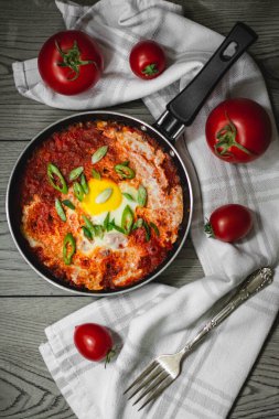 Shakshuka geleneksel orta doğu yemeği domates ve yumurtalarla küçük bir tavada soğan ve biberle süslenmiş. Arka planda domatesler, karanlık ve karamsar konsept