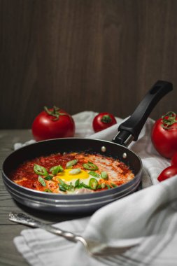 Shakshuka geleneksel orta doğu yemeği domates ve yumurtalarla küçük bir tavada soğan ve biberle süslenmiş. Arka planda domatesler, karanlık ve karamsar konsept