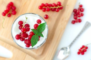 Granola ile hafif yaz kahvaltısı parfe, vegan Yunan yoğurdu, kırmızı frenk üzümü ve fesleğen yapraklarıyla süslenmiş. Hafif ve havadar estetik