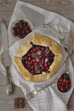 Koyu çikolata ve ekşi vişneli turta. Koyu ve kasvetli atmosferde. Kirazlar ve eski çatal bıçaklarla çevrili.