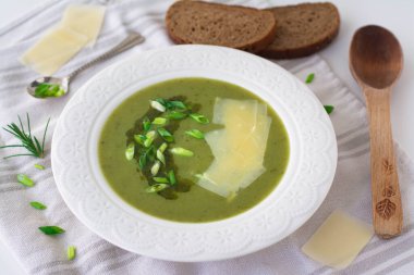 Pırasa çorbası, soğan soğanı yeşil soğan ve pesto, soğan ve tıraş edilmiş parmesan peyniri ile süslenmiş patates. Arka planda siyah çavdar ekmeği, ahşap kaşık ve tıraş edilmiş parmesan peyniri var.