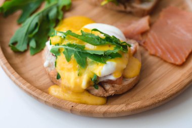 Haşlanmış Benedict usulü yumurta, Hollandaise sosu, füme somon, roka ve kızarmış ekmek. Tahta plaka, beyaz arkaplan.