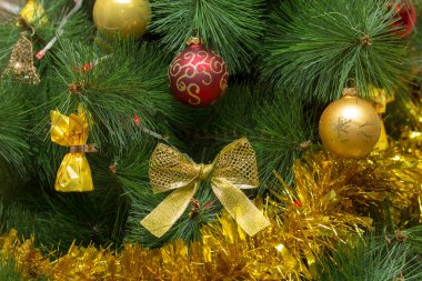 Yeşil Noel ağacı zengin kırmızı ve altın parlak ve mat cam topları, narin sarı yay ve çikolata ile kıyafeti