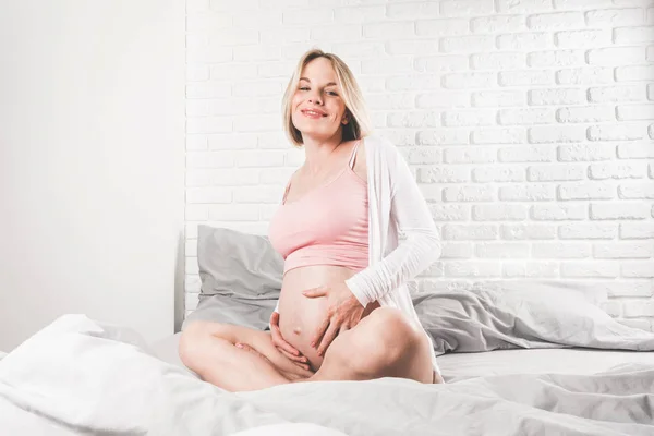 Jovem grávida feliz encontra-se na cama e acaricia sua barriga . — Fotografia de Stock