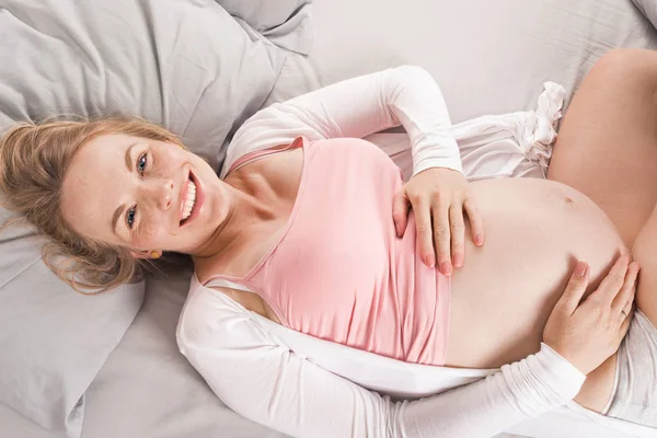 Счастливая беременная женщина лежит в постели и мечтает о своем будущем ребенке. Вид сверху — стоковое фото