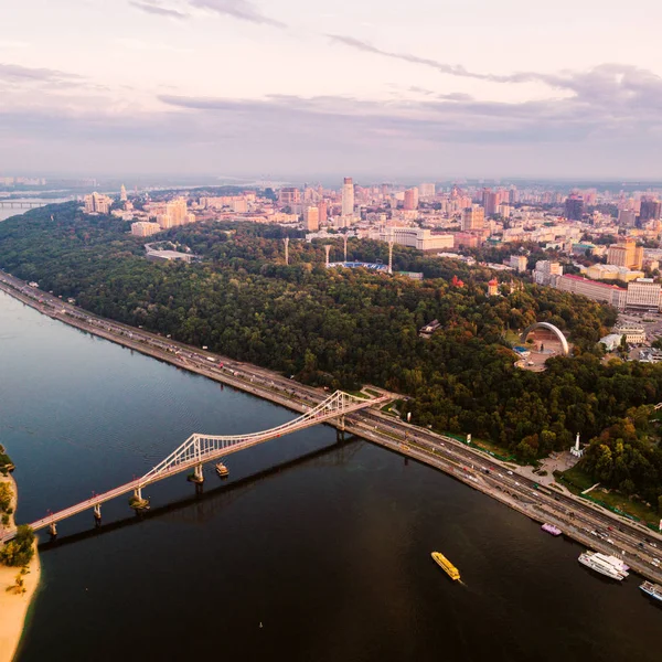 Vista panoramica del quartiere Podol, del centro città e Vladimirskaya Gorka. Vista generale della riva destra di Kiev con il fiume Dnieper, un ponte pedonale e una grande area parco al tramonto . — Foto Stock