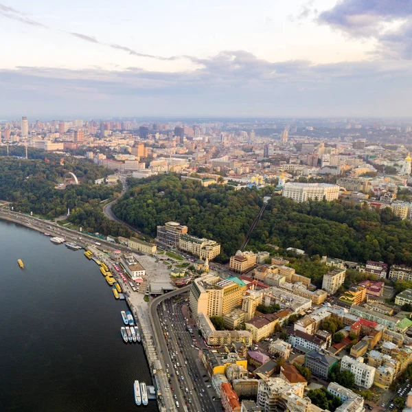 Panoramic view of the Podol district, city center and Vladimirskaya Gorka. General view of the right bank of Kiev with the Dnieper River, a pedestrian bridge and a large park area at sunset. — Stock Photo, Image