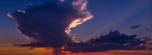 Céu bonito ao pôr-do-sol com uma enorme nuvem em cores laranja escuro e azul escuro — Fotografia de Stock