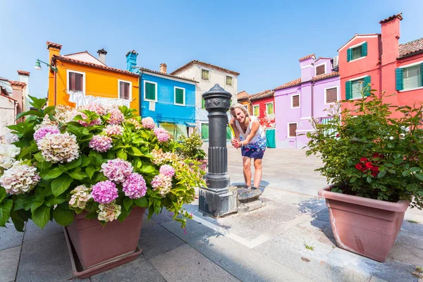 Female traveler stands near a column with water in a courtyard on the island of Burano, Venice, Italy