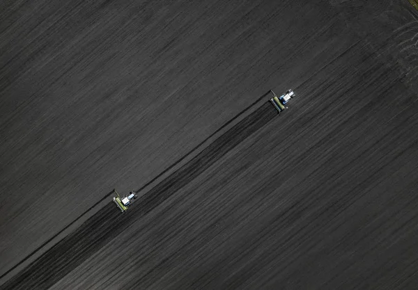 Two bright blue tractors plowing the ground against a black earth background. Top view