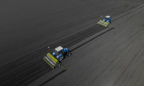 Dos tractores azules brillantes arando el suelo sobre un fondo negro de tierra . — Foto de Stock