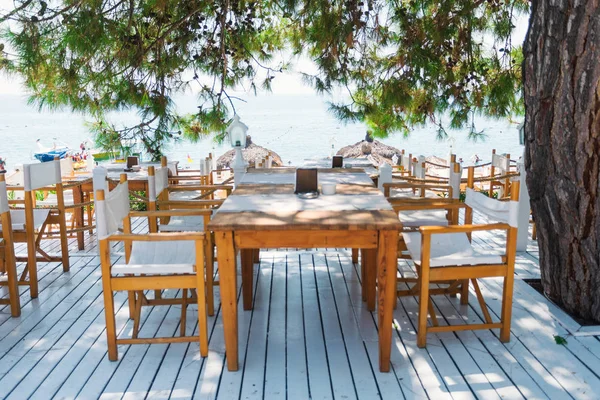 Restaurante con mesas en una terraza blanca como la nieve con vistas al mar bajo ramas de pino . — Foto de Stock