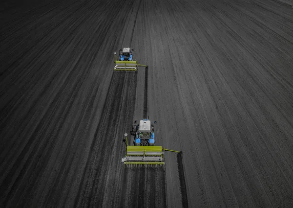 Два яскраво-блакитних трактора, що оранюють землю на фоні чорної землі . — стокове фото