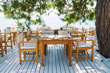 Çamın dalları altında denize bakan bembeyaz bir teras üzerinde tablolarla Restoran.