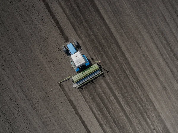 Ярко-синий трактор, вспахивающий землю на черноземном фоне. Вид сверху — стоковое фото