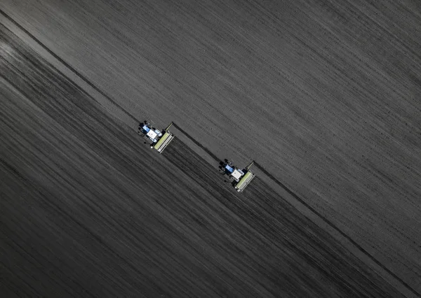 Two bright blue tractors plowing the ground against a black earth background. Top view