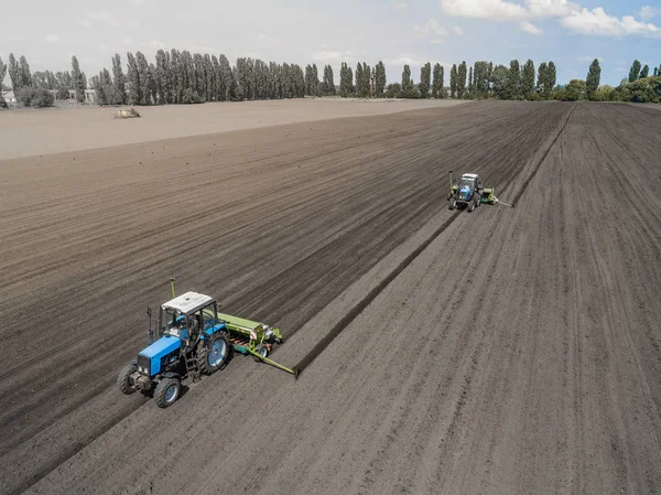 Two bright blue tractor plowing the ground against a black earth background.