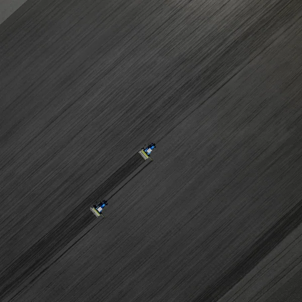 Zwei leuchtend blaue Traktoren pflügen den Boden vor schwarzem Erdboden. Ansicht von oben — Stockfoto