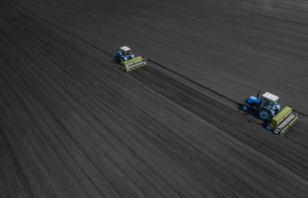 Zwei hellblaue Traktoren pflügen den Boden vor schwarzem Erdhintergrund. — Stockfoto