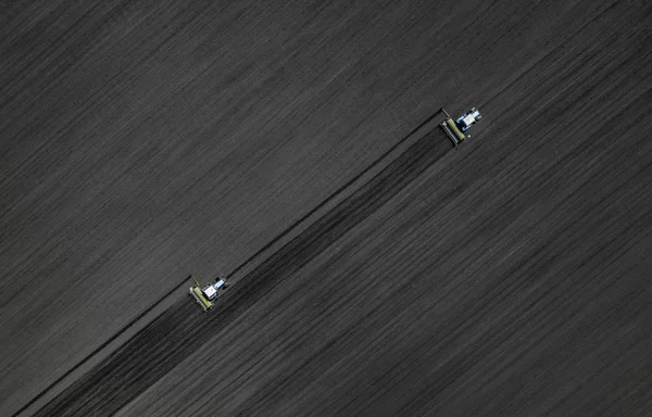 Dos tractores azules brillantes arando el suelo sobre un fondo negro de tierra. Vista superior —  Fotos de Stock