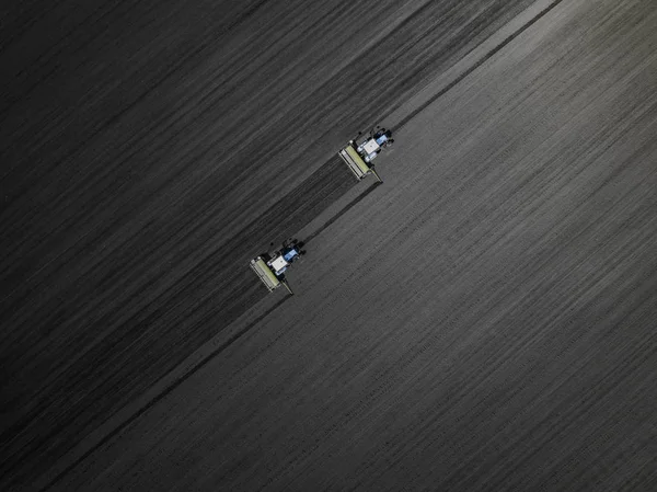 Dois tratores azuis brilhantes a arar o chão contra um fundo de terra preta. Vista superior — Fotografia de Stock