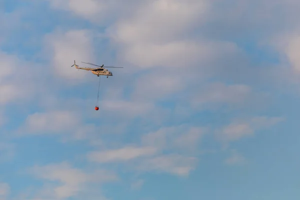 Helikopter strażak z pełnym koszem Woda leci przed piękne niebo — Zdjęcie stockowe