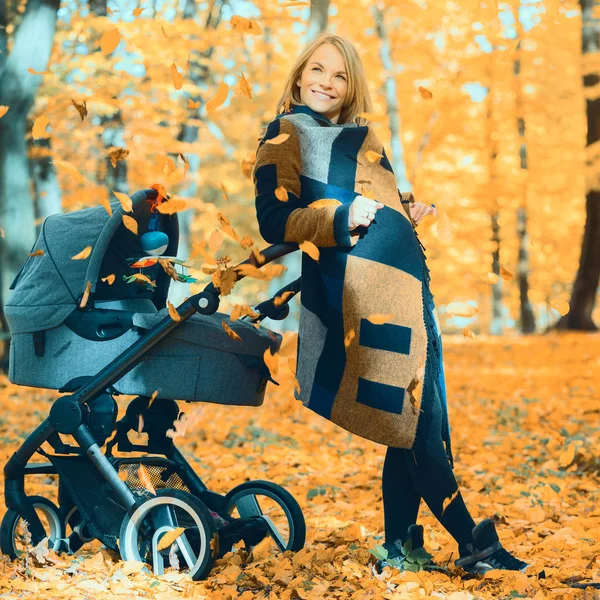 A young mother with a stroller is talking on her mobile phone while walking in the park — Stock Photo, Image