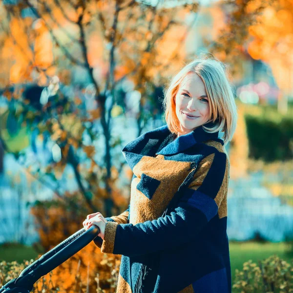 Una joven madre con un cochecito pasea por el parque de otoño —  Fotos de Stock